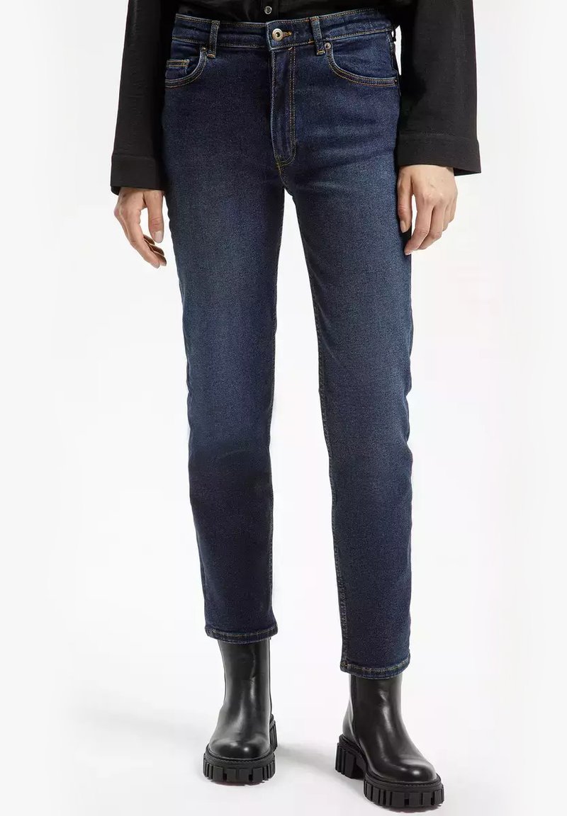 Granatowe dżinsy o slim fit, pięć kieszeni, kontrastowe przeszycia i nadstawka. W połączeniu z czarnymi botkami do kostki.