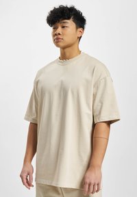 Beige oversize t-shirt lavet af blød bomuld. Har korte ærmer, en rund hals og en afslappet pasform med minimale syninger.