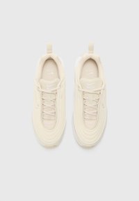 Bežiniai Nike Air Max 97 sportbačiai su tekstūruotu paviršiumi, suapvalintu pirštu ir baltais akcentais. Yra raištelių užsegimas ir kilpa ant kulno.