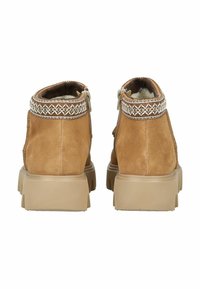 Bottes chelsea en suede marron avec une finition texturée, des coutures décoratives au col et une semelle extérieure en caoutchouc robuste. Fermeture par zip à l'arrière.