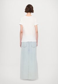 Tricou alb cu mânecă scurtă, asortat cu o fustă maxi din denim de culoare albastru deschis. Fusta are buzunare la spate și o siluetă dreaptă.