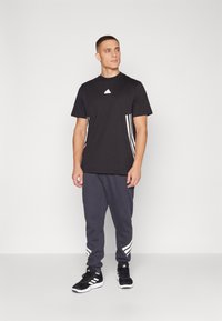Black crew neck t-shirt with white logo and three vertical white stripes on sides, paired with gray sweatpants featuring striped accents.