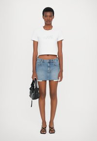 Tricou alb scurt cu logo, fustă mini din denim cu talie înaltă, sandale negre cu curea și o mică geantă neagră cu un model texturat.