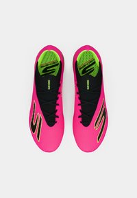 Jasně růžové sportovní boty s texturovaným povrchem, černými doplňky, černými tkaničkami a neonově zeleným vnitřním lemováním. Mají charakteristický design loga.