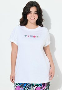T-shirt en coton blanc avec des manches roulées et cinq symboles colorés brodés : cœur, étoile, carré, smiley et triangle.