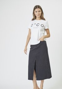 Camiseta blanca con texto negro "C°C LOVE AND JOY" combinada con una falda de mezclilla oscura hasta el tobillo con una abertura frontal y una textura suave.