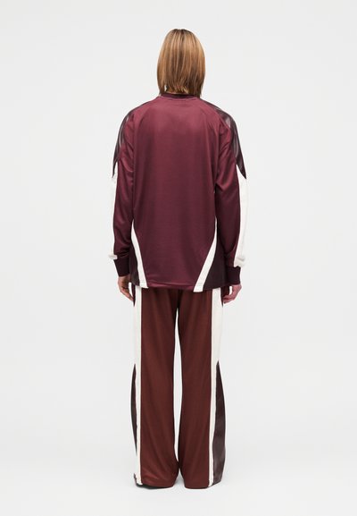 Tenue de sport composée d'un haut à manches longues bordeaux et d'un pantalon à jambes larges avec des panneaux latéraux crème, réalisé en tissu lisse et léger.