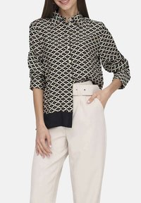 Chemise à boutonner crème et marine avec un motif géométrique. Dispose d'un col, de manches longues et d'un ourlet inférieur uni marine. Texture lisse.