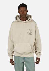 Sweatshirt bege com capuz, feito de algodão, apresentando um bolso frontal e texto do logótipo no peito. Textura suave com punhos e bainha ribados.