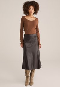 Braunes langärmliges Oberteil kombiniert mit einem dunkelbraunen Leder-A-Linienrock. Das Outfit zeichnet sich durch glatte Texturen und vertikale Nahtdetails aus.
