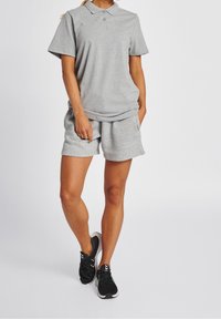 Szara koszulka polo z krótkim rękawem, zestawiona z pasującymi szarymi szortami oraz czarnymi butami sportowymi z białymi akcentami. Zestaw casualowej odzieży sportowej.