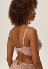 Różowy biustonosz z koronką i gładkim materiałem, z regulowanymi ramiączkami, zapięciem na haftki oraz kwiatowymi detalami koronkowymi wzdłuż pleców i krawędzi.
