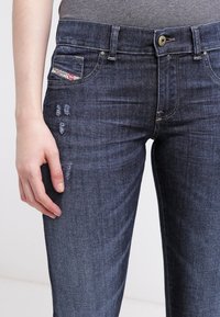 Jeans in denim blu scuro con dettagli strappati nella parte frontale, design classico a cinque tasche e chiusura con un solo bottone in vita.