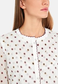 Weiße Bluse mit mehrfarbigen Punkten in Rosa, Gold und Schwarz. Mit welligem Kragen und Knopfschluss. Leichtes Material.