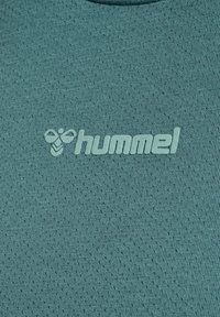 Tissu de sport bleu sarcelle avec de petites perforations, présentant le logo blanc "hummel" et l'icône de l'abeille centrés sur la surface.