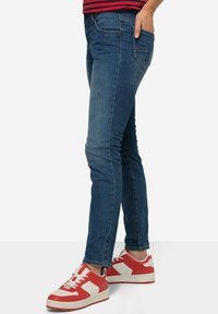 Tummansiniset farkku skinny jeansit, joissa on sileä pinta, klassinen viisi-taskuinen muotoilu ja huomaamatonta ompelua, yhdistettynä punavalkoisiin lenkkareihin.