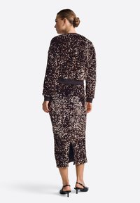 Sötét tónusú, flitterekkel díszített zakó és szoknya, testre szabott kialakítással, bordás mandzsettával és hátsó hasítékkal. Fekete magassarkú cipővel párosítva.