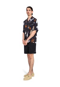 Camiseta negra de manga corta con impresiones gráficas de mariposas coloridas, combinada con pantalones cortos negros y zapatos de color claro. Diseño simple y casual.