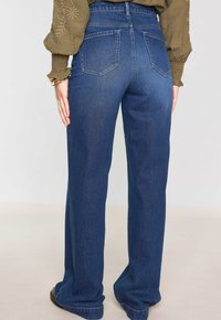 Jean en denim bleu avec une coupe droite, taille haute et design à cinq poches. Le tissu présente une texture subtile ; l'arrière comporte deux poches.