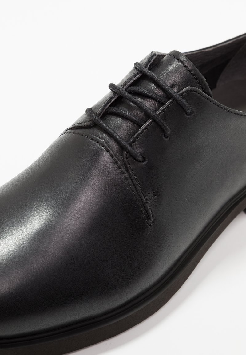 Schwarzer Lederschuh mit glatter Textur, runder Spitze und kontrastierenden Schnürsenkeln. Merkmale sind dezente Nähdetails und eine flache Sohle.