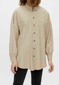 Beige rutmönstrad skjorta med krage, långa ärmar och knäppning fram. Har två bröstfickor och en rundad nederkant, tillverkad av ett mjukt material.