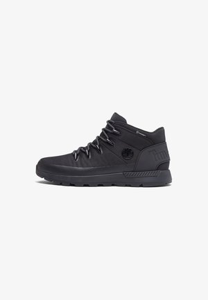 Zapatilla Timberland negra de corte medio con cierre de cordones, suela texturizada y logo de la marca en el lateral y el talón.