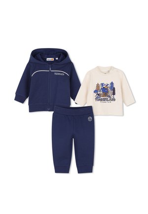 Conjunto para niño pequeño con chaqueta con capucha azul marino con cremallera, camiseta de manga larga color crema con estampado de cabaña y árboles, y pantalones azul marino con cintura elástica.