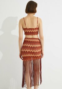Zwei-Teile-Outfit mit einem rot-orangenen gemusterten Crop-Top mit dünnen Trägern und einem passenden Rock mit Fransen-Details.