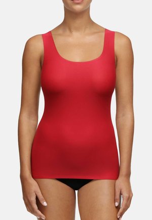 Κόκκινο αμάνικο τοπ με στρογγυλή λαιμόκοψη, κατασκευασμένο από ομαλό, ελαστικό υλικό; εφαρμοστή γραμμή με μήκος μέχρι το ύψος των γοφών, σε συνδυασμό με μαύρα παντελόνια.