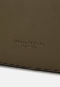 Oliivinvihreä nahkalaukku, jossa on teksturoitu pinta, varustettu kohokuvioidulla "Marc O'Polo" -logolla ja "EST. IN STOCKHOLM" -yksityiskohdalla.