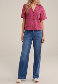 Kortärmad, V-ringad skjorta i rosa broderad tyg, kombinerad med vida blå jeans. Toppens design har dekorativa hål och knappar.