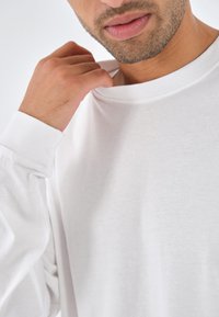 Witte langarm t-shirt met gebreide halslijn en manchetten, met een zachte, gladde katoenen textuur en een ontspannen pasvorm. Draagt nauw rond de hals.