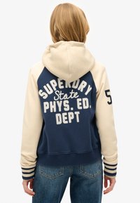 Navyblauwe en crèmekleurige hoodie met kleurvlakken en geborduurde tekst. Voorzien van een capuchon met trekkoord, geribbelde manchetten en een ontspannen pasvorm.