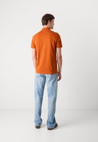 Oransje kortermet polo skjorte med rett kant, sammen med lyseblå jeans. Designet har standard krage og myk tekstur.