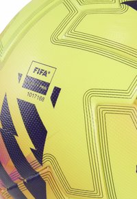 Pallone da calcio giallo con superficie texturizzata, linee nere e audaci motivi grafici. Mostra il logo FIFA e la certificazione di qualità.