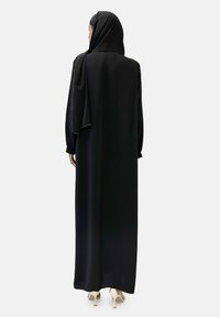 Abaya noire à manches longues en tissu lisse, présentant une silhouette fluide, accompagnée d'un hijab noir assorti orné de détails subtils.