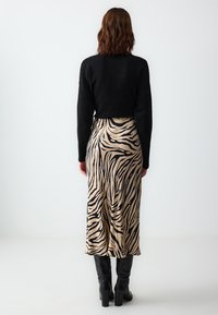 Maglione nero e gonna beige di lunghezza media con strisce a tigre nere. L'outfit presenta una texture morbida e una silhouette elegante.