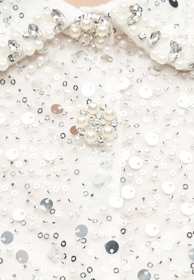 Tissu blanc orné de sequins argentés, de petites perles transparentes et de boutons en perle décorés de strass.