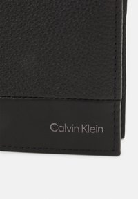 Portafoglio in pelle nera con superficie testurizzata, bordi cuciti e logo Calvin Klein argentato in basso.