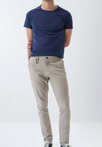 Námořnické tričko s krátkým rukávem v kombinaci s světle béžovými kalhotami. Kalhoty mají očka na opasek a detail karabiny s hladkým povrchem.