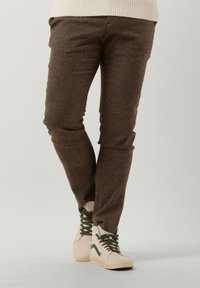 Brown textured trousers with a slim fit, paired with light sneakers featuring green accents and classic lacing.