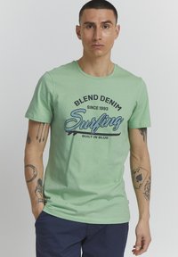 Mintově zelené bavlněné tričko s grafickým potiskem obsahujícím text "Surfing" a "Blend Denim". Krátké rukávy, kulatý výstřih a volný střih.