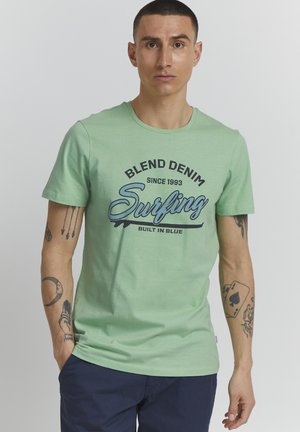 Mintgrøn bomulds T-shirt med et grafisk print med teksten "Surfing" og "Blend Denim". Korte ærmer, rund halsudskæring og afslappet pasform.