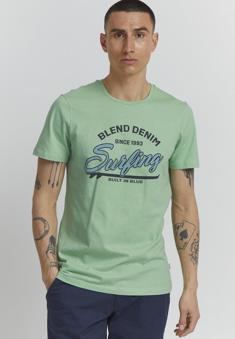 Mintově zelené bavlněné tričko s grafickým potiskem obsahujícím text "Surfing" a "Blend Denim". Krátké rukávy, kulatý výstřih a volný střih.