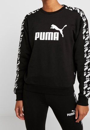 Person wearing black Puma sweatshirt and leggings with white Puma logo on chest, sleeves, and thigh.
