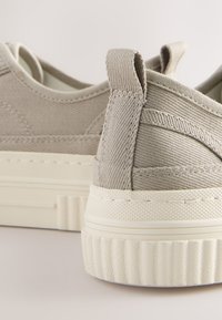 Grijze canvas sneakers met een gestructureerde stof en crèmekleurige rubberen zolen. Kenmerken zijn onder meer een gestikt ontwerp en een lus aan de achterkant voor gemakkelijk aan- en uittrekken.
