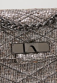 Bolso de mano de tweed metálico con un patrón acolchado, una correa de cadena plateada y un cierre metálico elegante con marcas grabadas.