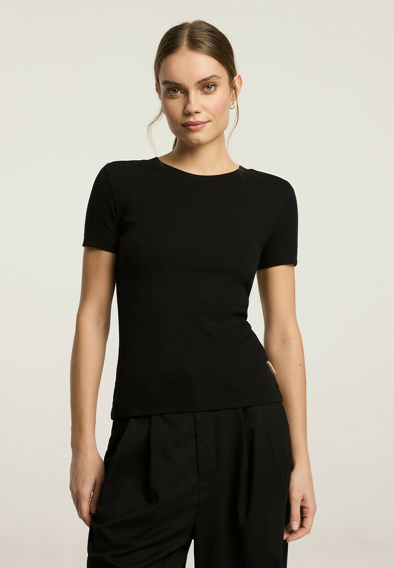 Czarny, dopasowany top z krótkim rękawem, z teksturą prążkowaną, okrągły dekolt, w połączeniu z luźnymi czarnymi spodniami. Minimalistyczny design, bez widocznych wzorów lub grafik.