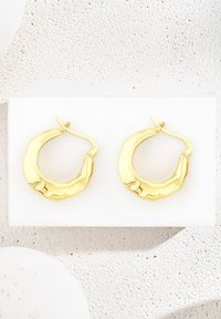 Guld örhängen med en texturerad, vågig design. Utrustade med en låsspärr och en polerad yta, uppvisade mot en vit bakgrund.