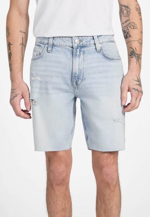 Shorts en denim bleu clair avec un design déchiré, présentant des ourlets effilochés et des détails de couture visibles. Portés avec un t-shirt blanc uni.